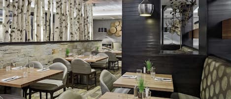 A restaurant interior with wooden tables, cushioned booths, and a stone wall.
