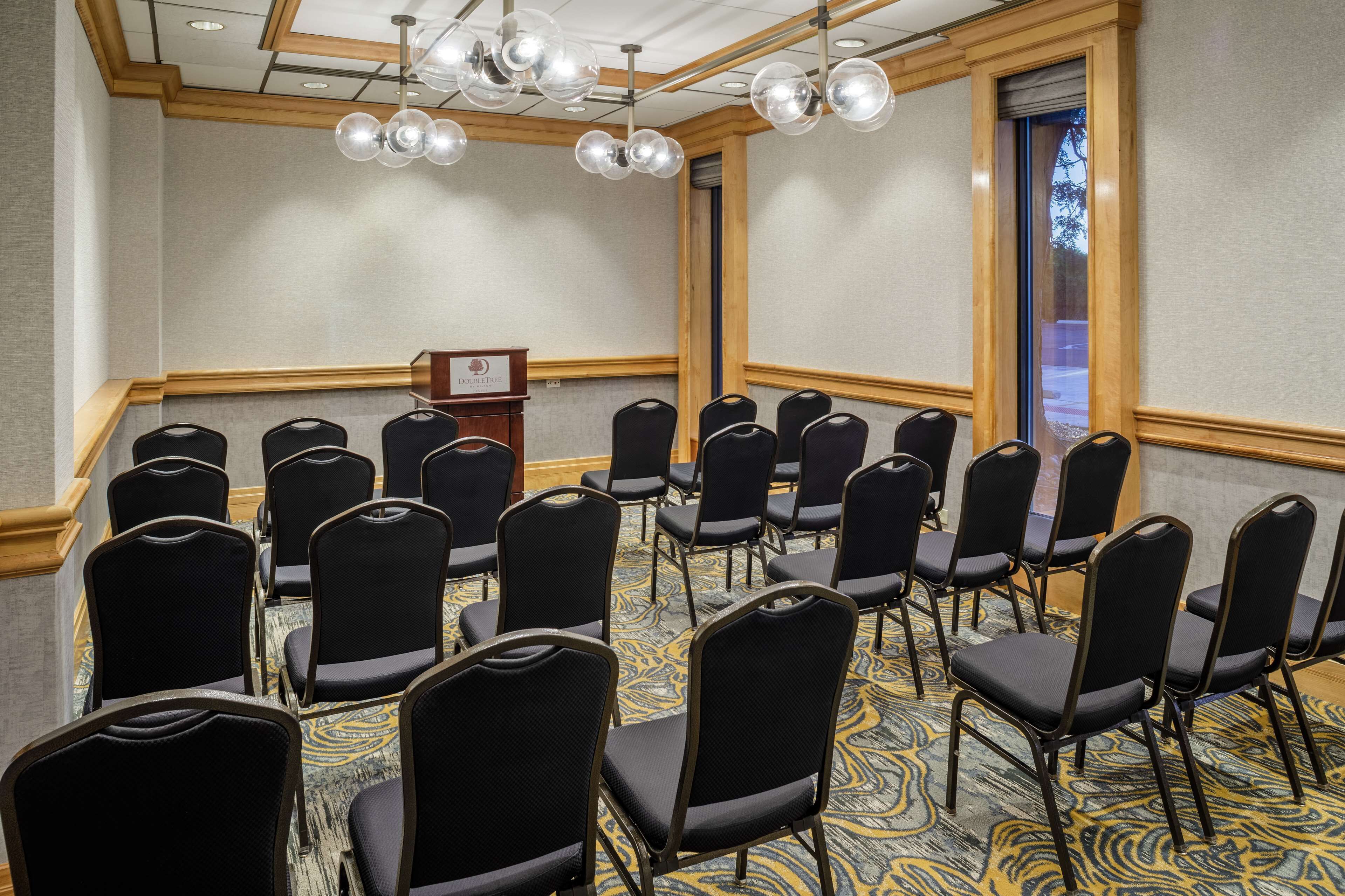 A conference room with rows of black chairs, a podium, and a patterned carpet.