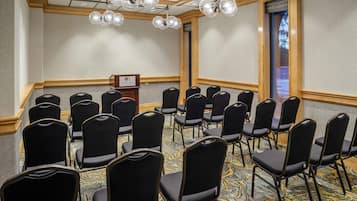 Un salón de conferencias con filas de sillas negras, un atril y una alfombra estampada.