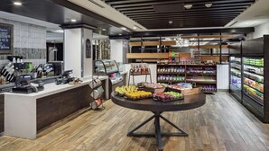 Une épicerie moderne avec un présentoir central de fruits et légumes, un rayon réfrigéré sur la droite et une zone de caisses sur la gauche.