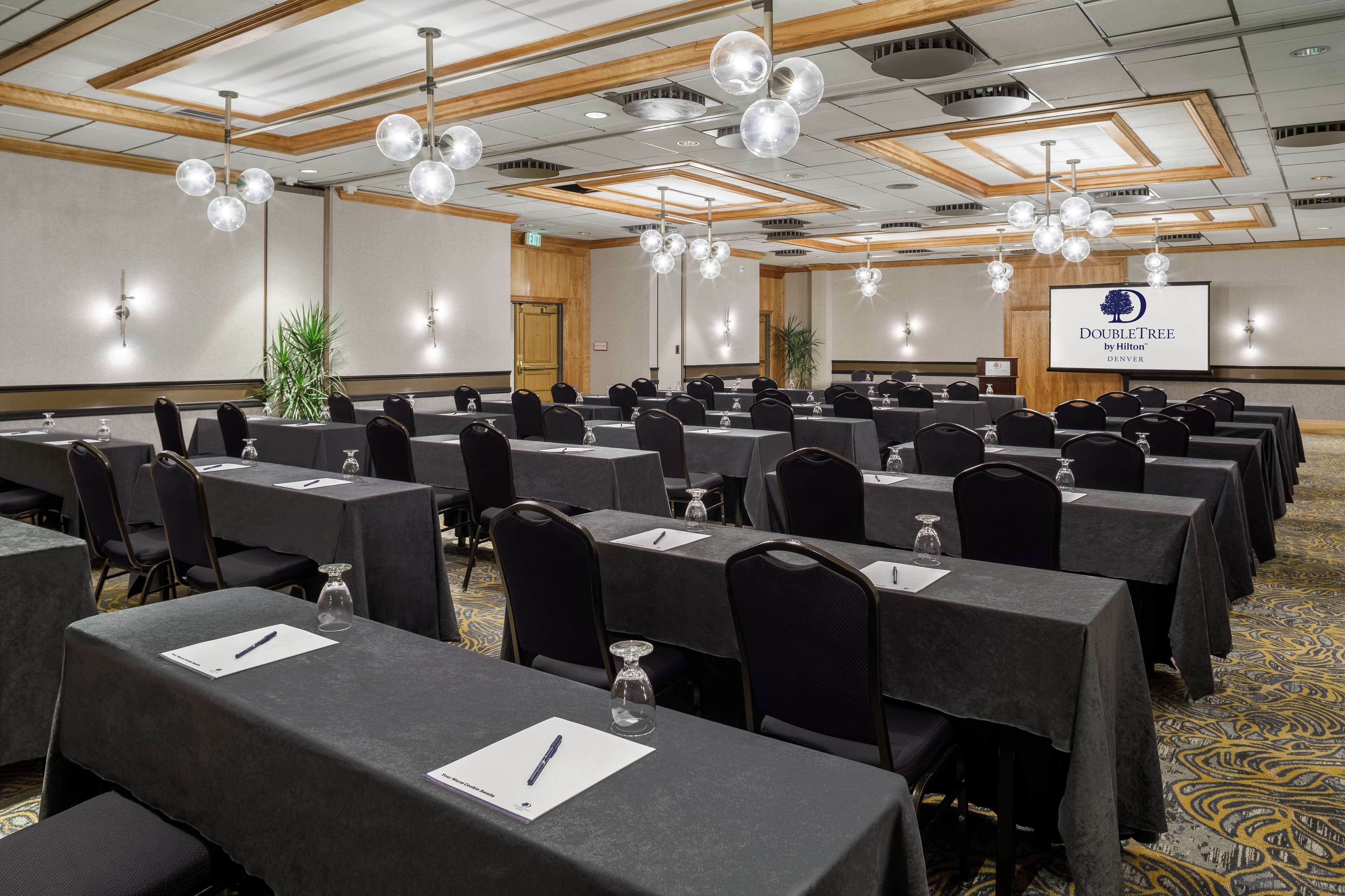 A conference room with multiple tables, chairs, and a large screen displaying the DoubleTree by Hilton logo.