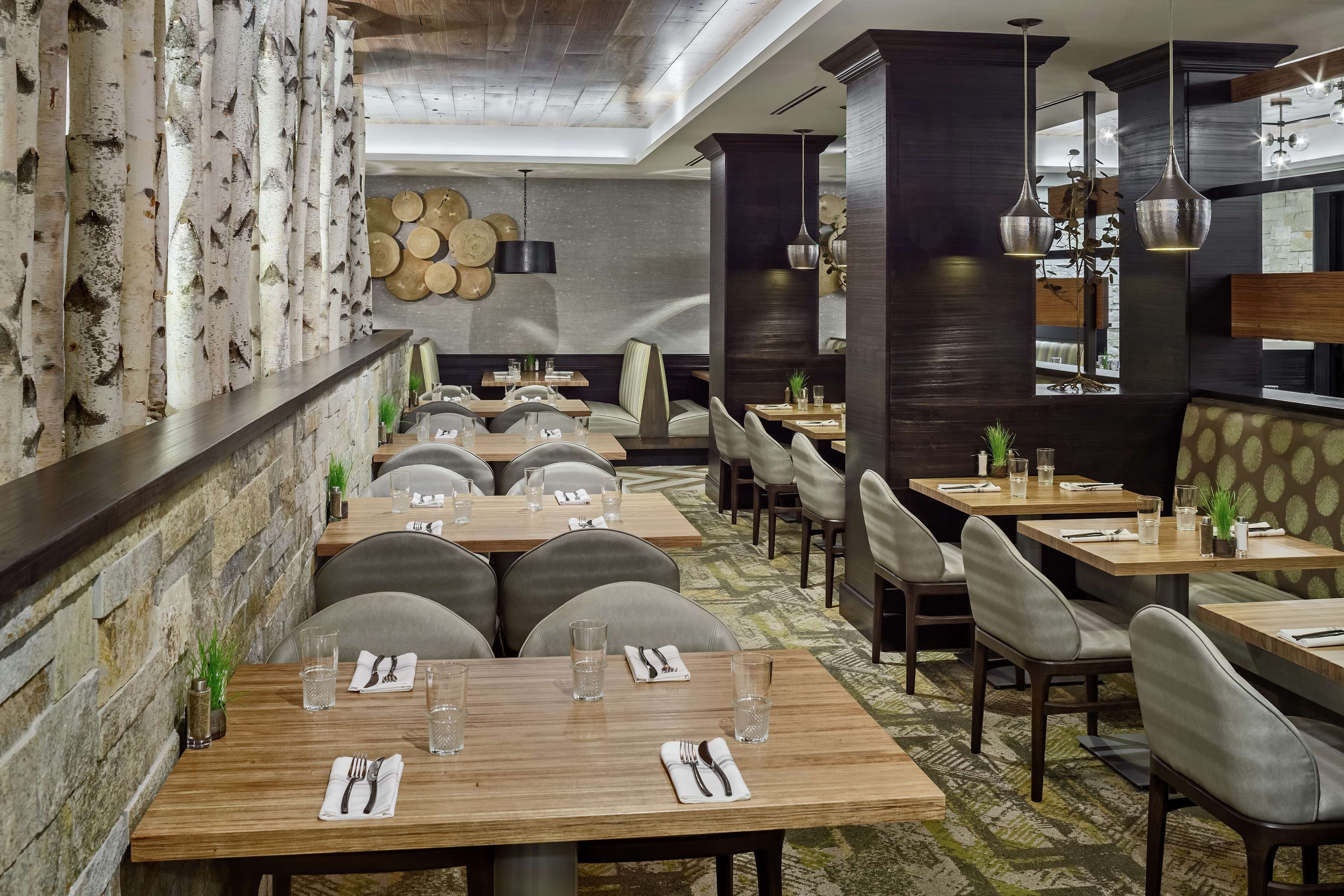 A restaurant with wooden tables and chairs, stone walls, and hanging pendant lights.