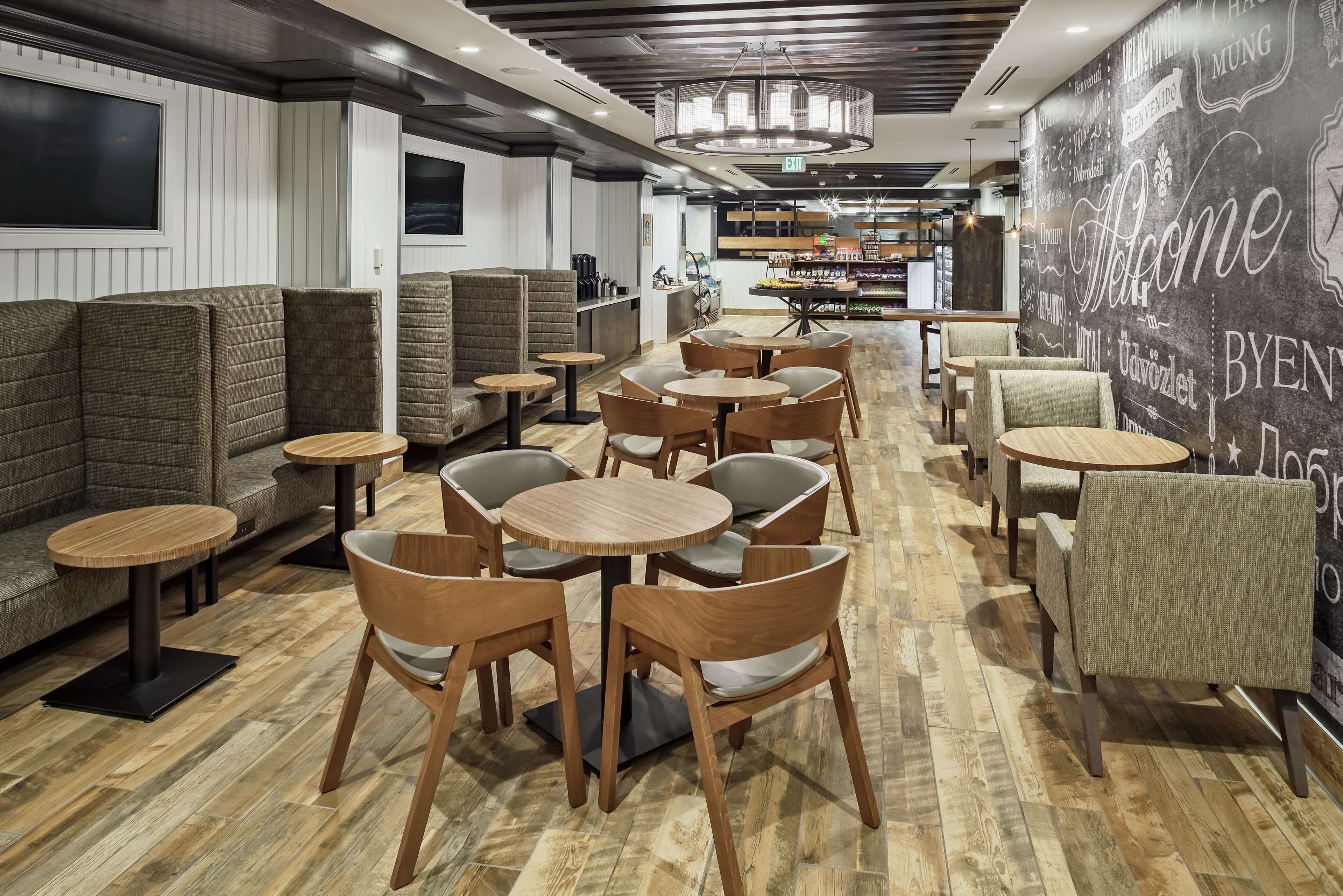 Ein modernes Café-Interieur mit Holztischen und -stühlen, einer Bar und einer Wand mit den Schriftzügen 'Welcome' und 'BYEN'.
