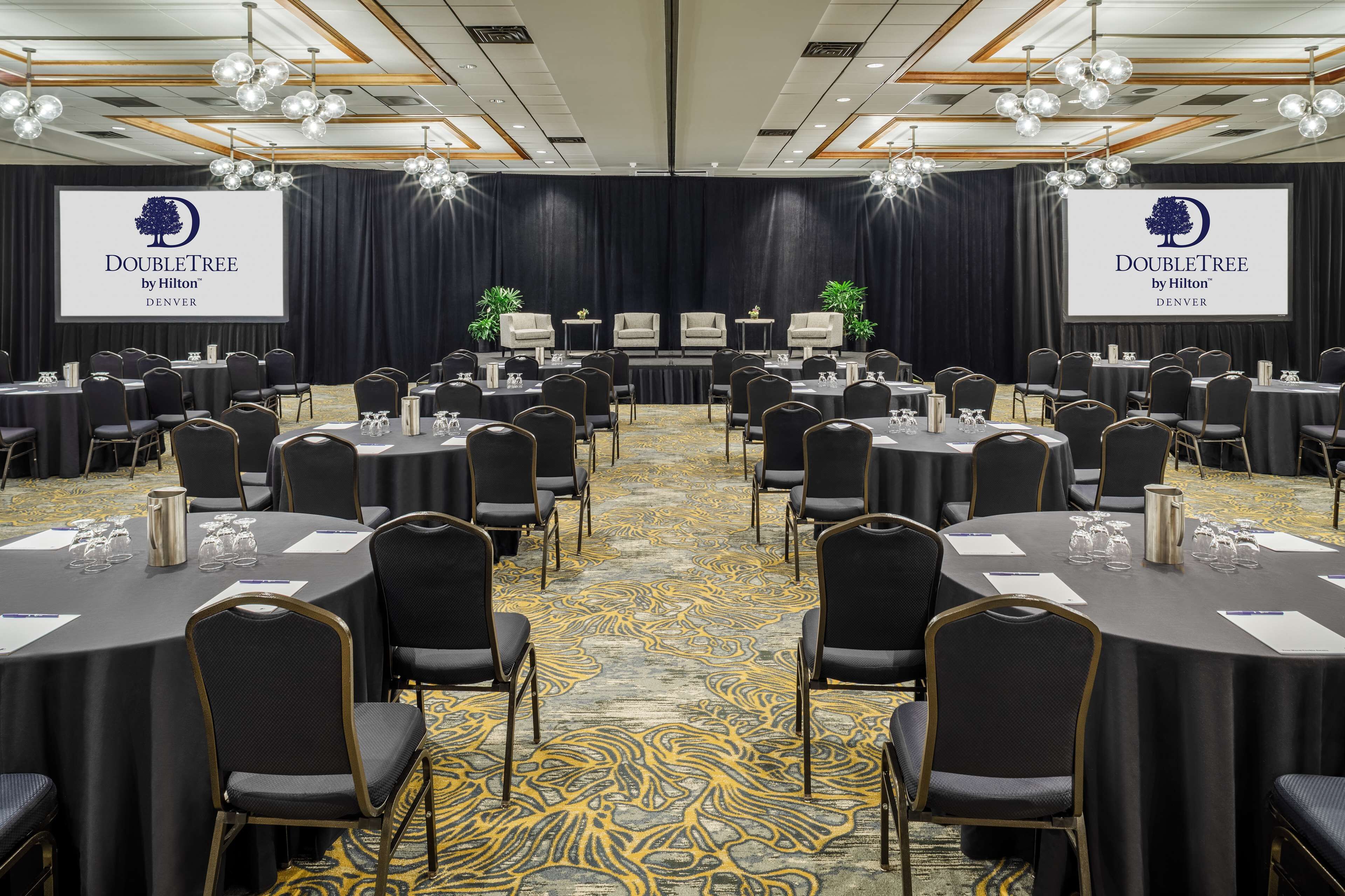A conference room with multiple tables and chairs, a large screen displaying the DoubleTree logo, and a carpeted floor.