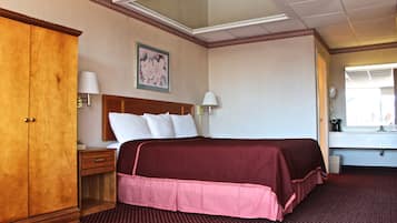 A hotel room with a large bed, a wooden wardrobe, a nightstand, a desk, a mirror, and a window.