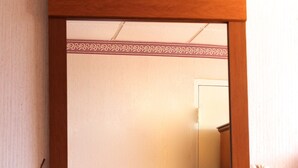 A large mirror with a wooden frame, a bed with a white pillow, and two vases with dried flowers on a wooden dresser.