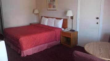 Quarto de hotel com uma cama grande, uma mesa de cabeceira com abajur, uma pequena mesa redonda e uma porta.