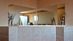 A bathroom with a large mirror, tiled walls, and two vases with dried plants.