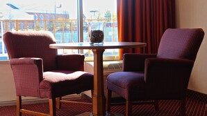 A hotel room with two patterned armchairs, a small round table, and a view of a building through a window.