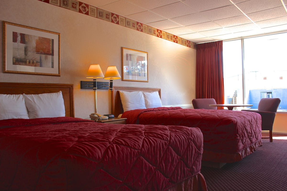 Habitación de hotel con dos camas, un escritorio, una silla y un ventanal grande.