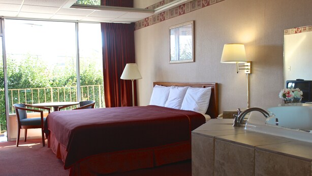 A hotel room with a bed, a desk, a chair, a bathroom, and a view of the outdoors.