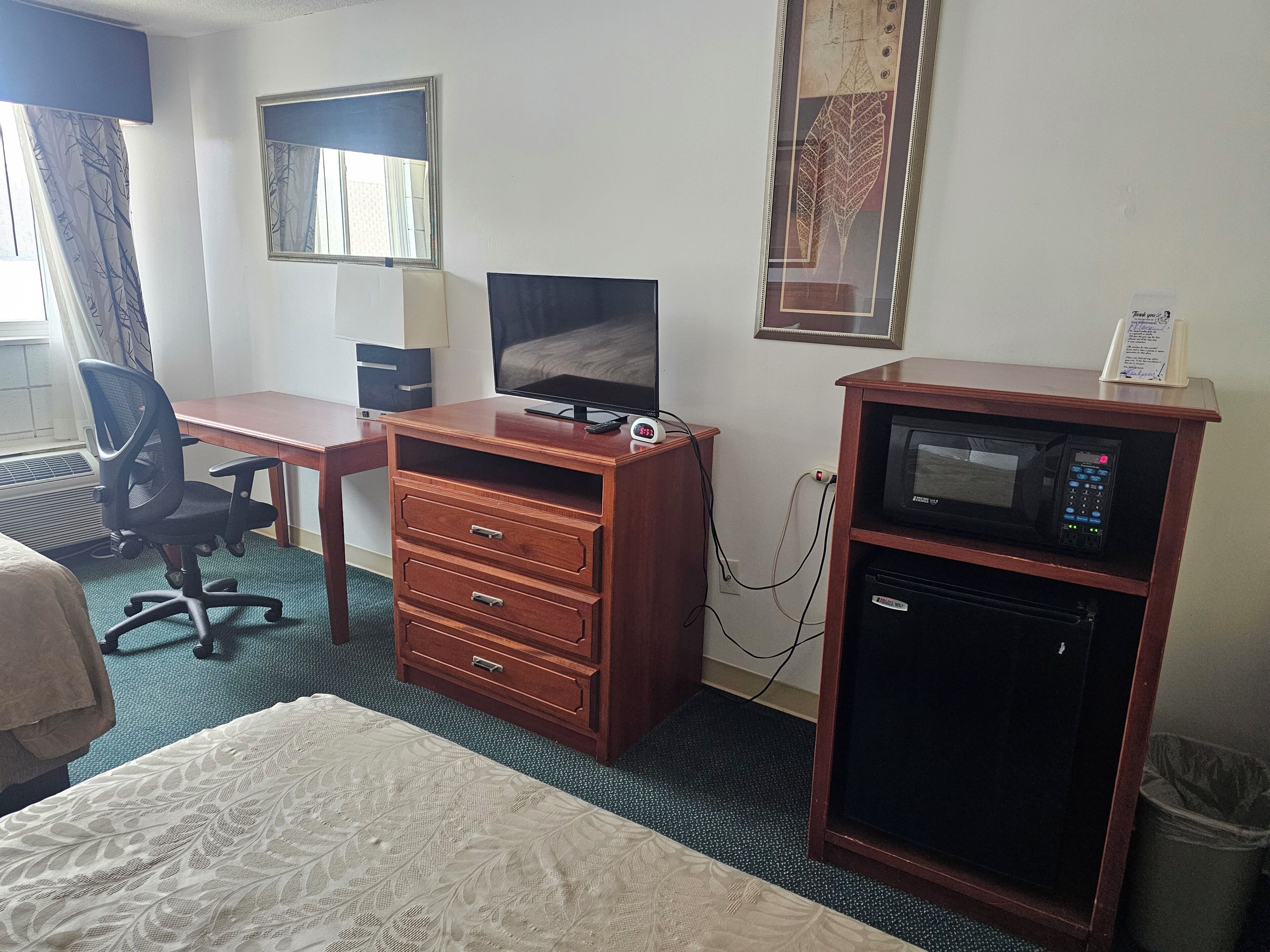 Quarto de hotel com cama, escrivaninha, computador, televisão, micro-ondas e lixeira.