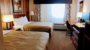 A hotel room with two beds, a desk, a chair, a TV, and a window with curtains.