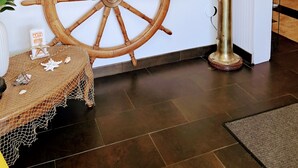 A room with a large wooden ship wheel, a brass ship's wheel, and a mural of a coastal scene.
