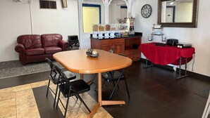 A dining area with a wooden table, black chairs, a red tablecloth, a leather sofa, and kitchen appliances.