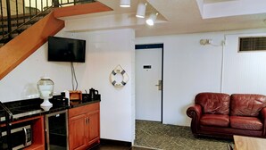 A living room with a wooden staircase, a kitchen area with a microwave, a television, and a leather sofa.