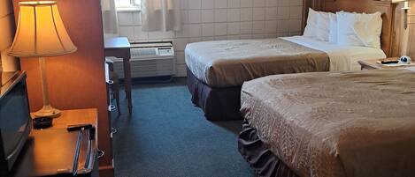 A hotel room with two beds, a desk with a lamp, a TV, and a window with curtains.