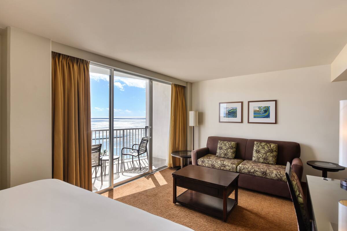 A hotel room with a balcony, a sofa, a coffee table, and a bed.