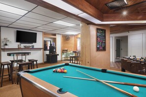A pool table with balls and cues, a television, and a chalkboard with writing.