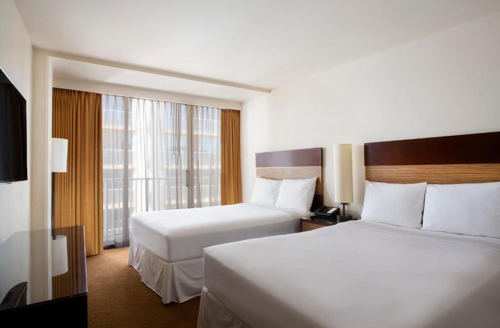 Una habitación de hotel con dos camas, televisión, escritorio y ventana con cortinas.