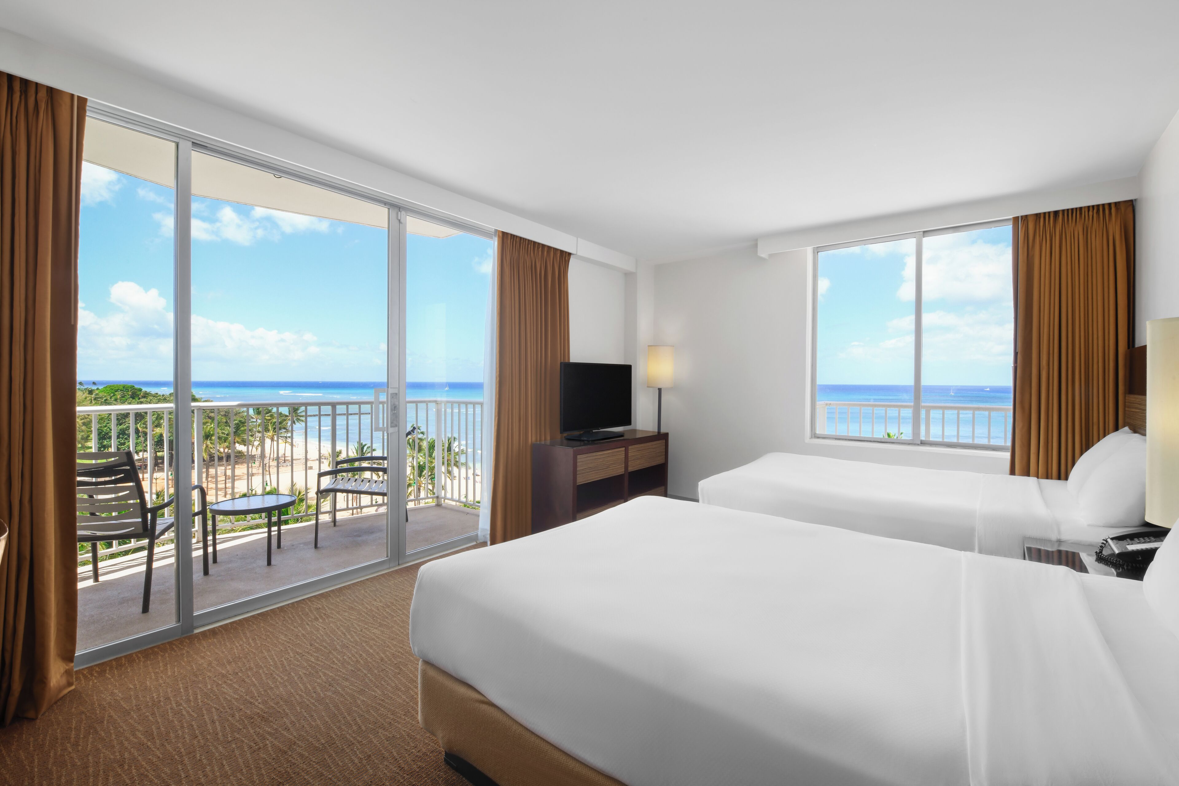 Une chambre d’hôtel avec deux lits, une télévision et un balcon offrant une vue sur la plage et l’océan.