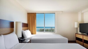 Une chambre d’hôtel avec deux lits, une télévision, un bureau et une fenêtre donnant sur la mer.