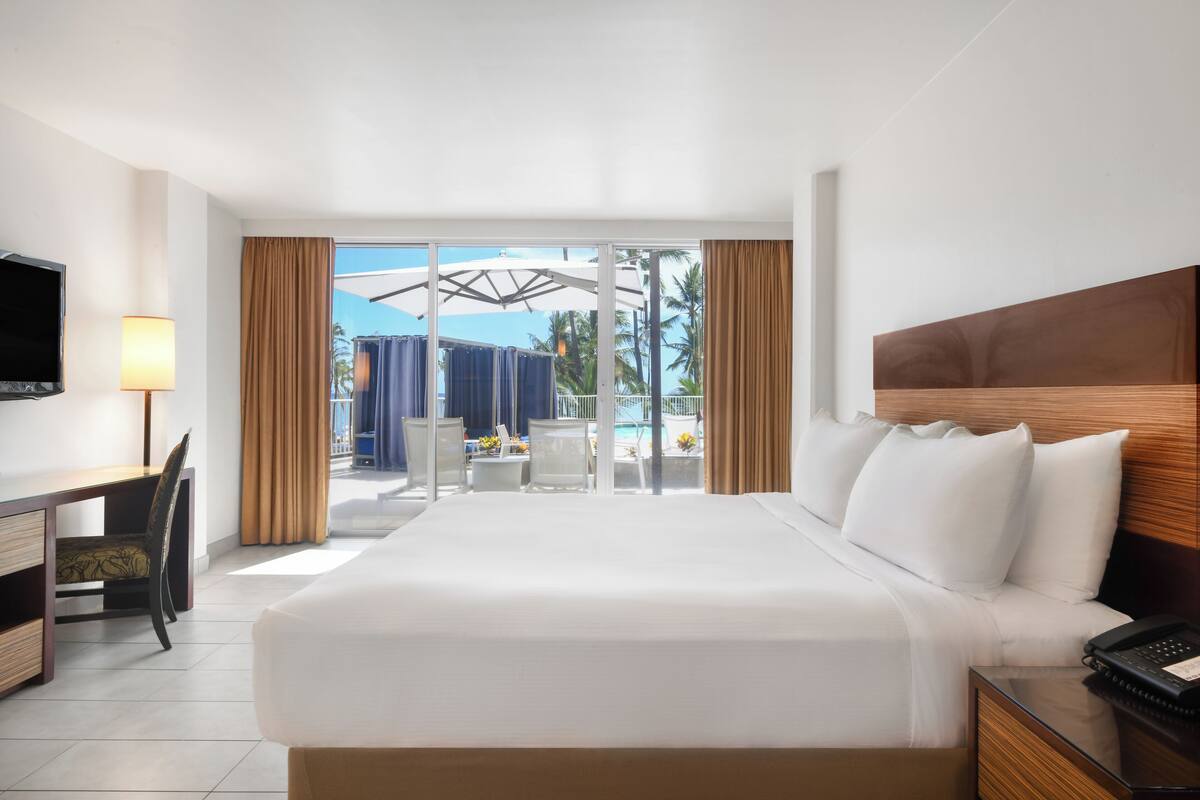 Une chambre d’hôtel avec un grand lit, un bureau avec une chaise, une télévision et une vue sur l’espace piscine.