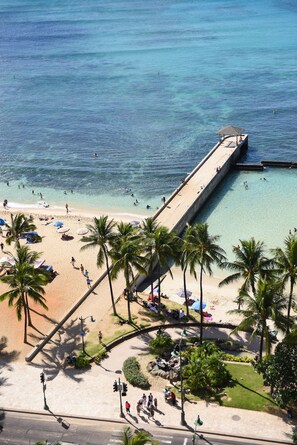 Ein Strand mit einem Steg, der sich ins Wasser erstreckt, Palmen und Menschen, die den Strand genießen.
