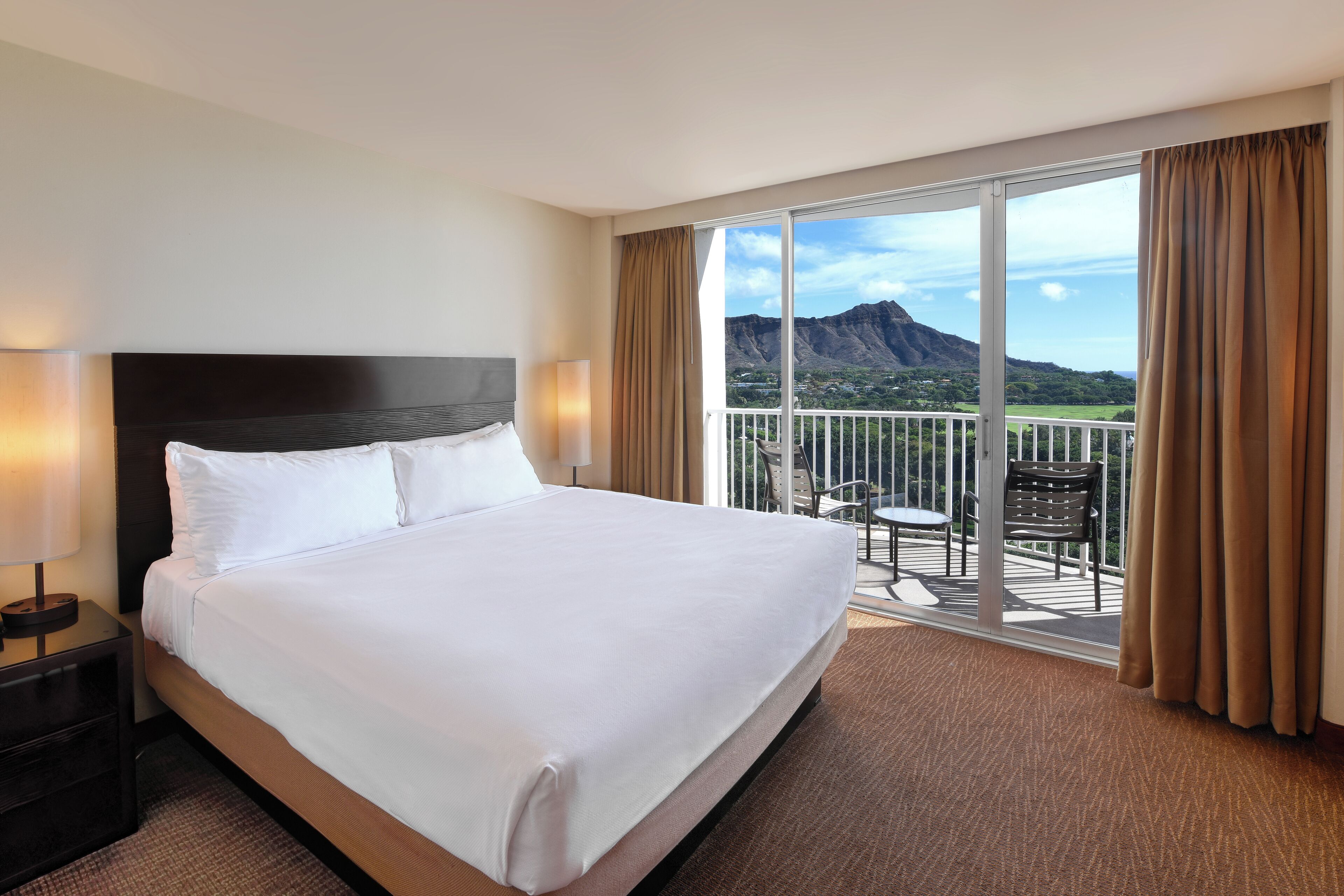 A hotel room with a large bed, a nightstand, a balcony with a view of mountains.
