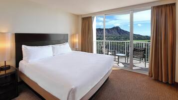 A hotel room with a large bed, a nightstand, a balcony with a view of mountains.