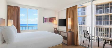 Habitación de hotel con cama, escritorio, silla, televisor y balcón con vista al océano.