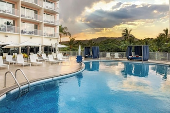 A hotel room with two beds, a TV, a desk, and a window with a view of the sea. at Park Shore Waikiki