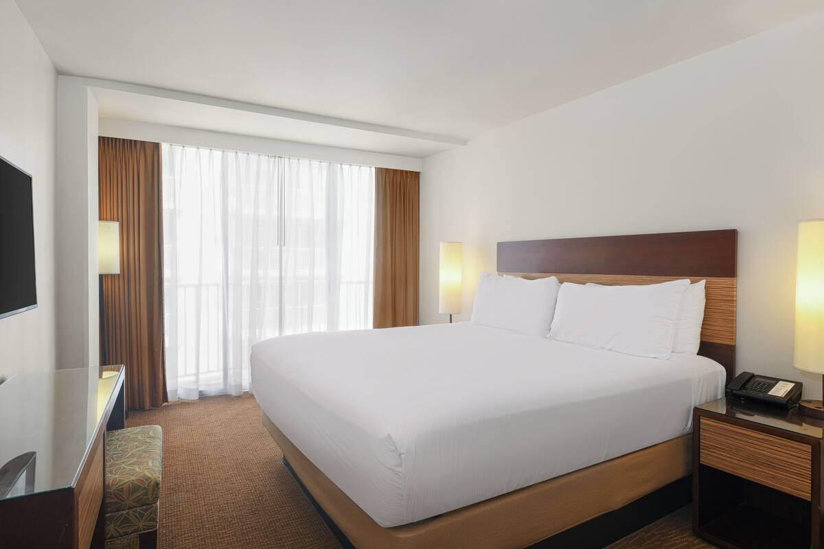 A hotel room with a large bed, bedside tables, a desk, and a TV.