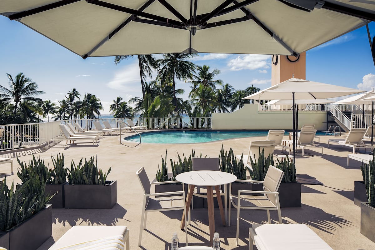 A poolside area with lounge chairs, a table, and umbrellas.