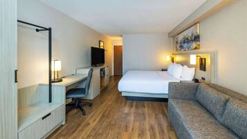 Una habitación de hotel con cama, escritorio con silla, televisor y sofá.