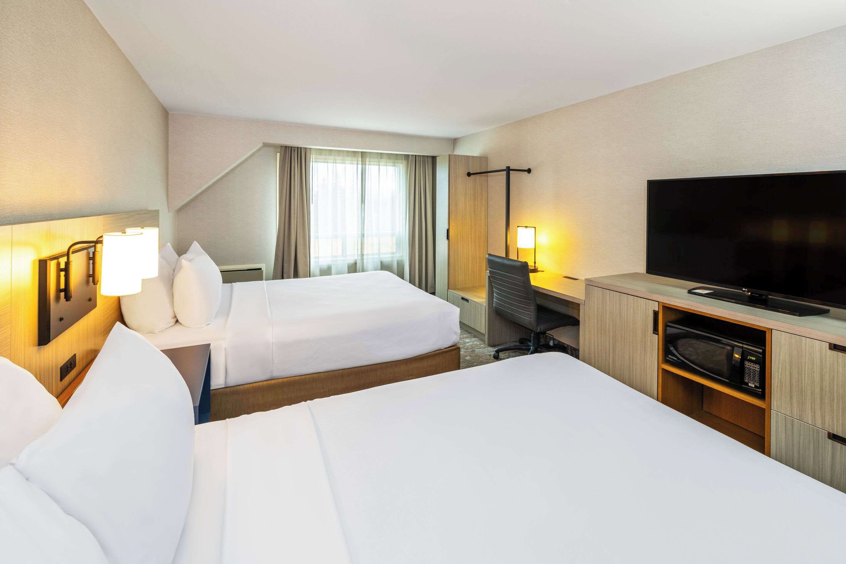 A hotel room with two beds, a desk, a television, and a microwave.