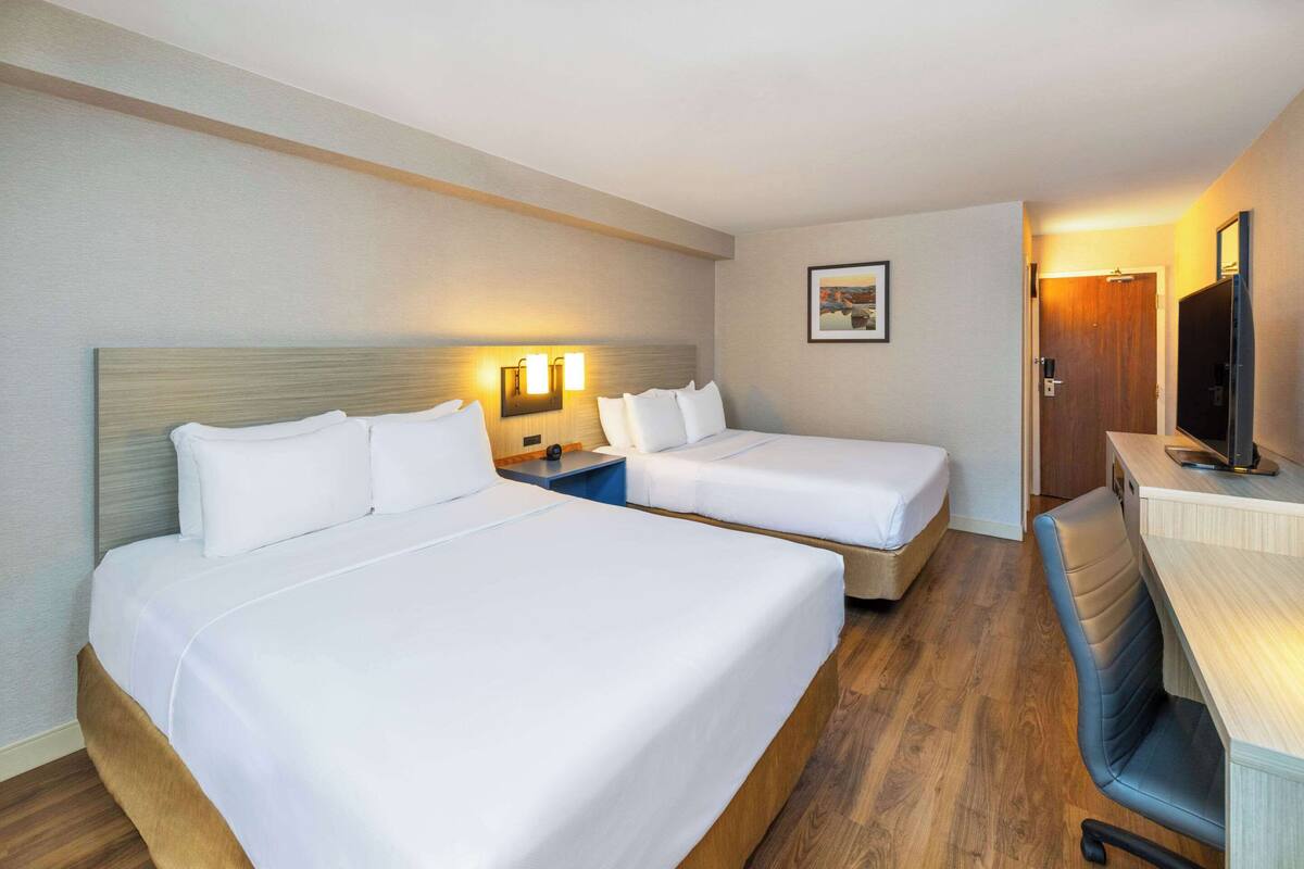 A hotel room with two beds, a desk, a chair, a TV, and a framed picture on the wall.