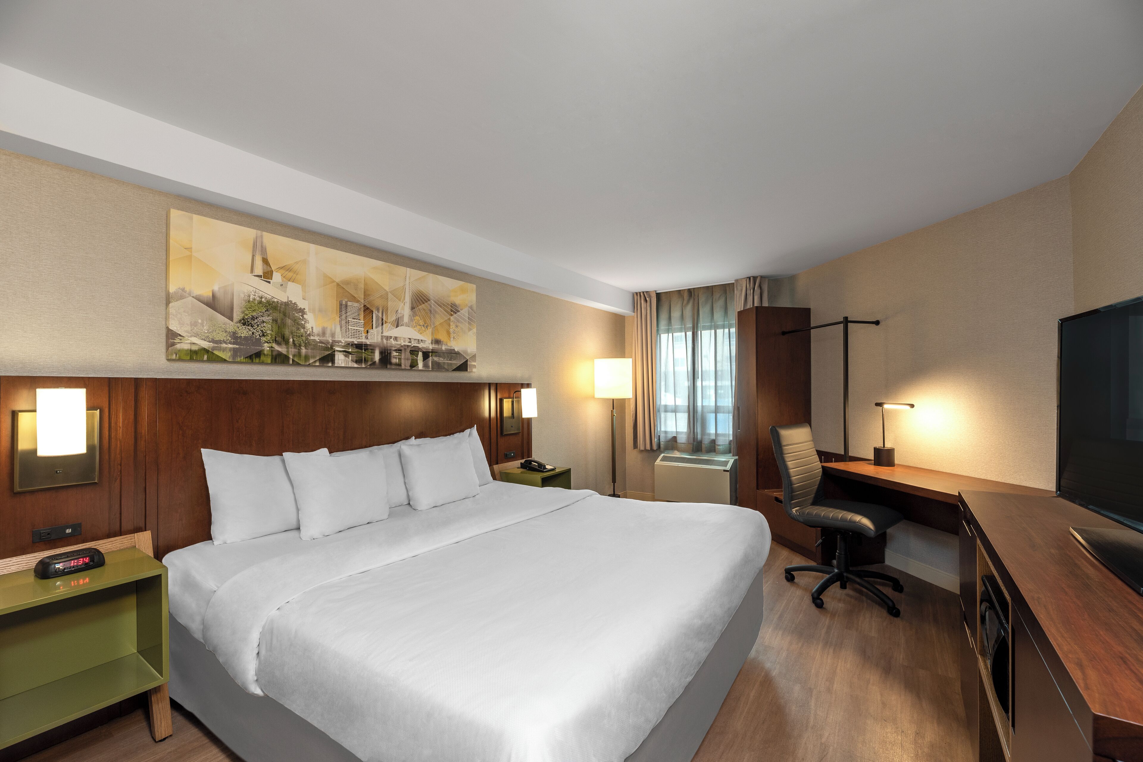 A hotel room with a large bed, a desk with a chair, a TV, and a painting on the wall.