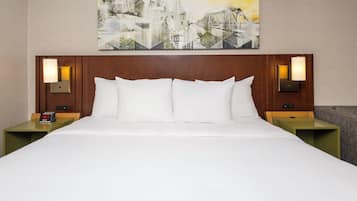 A hotel room with a large bed, two nightstands, a wall clock, and a painting above the bed.