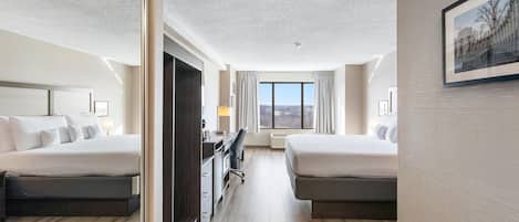 A hotel room with two beds, a desk, a chair, and a large window.