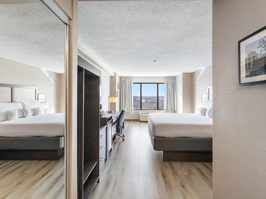 Habitació d'hotel amb dos llits, una taula de treball, una cadira i una finestra gran.