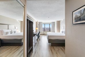 Habitación de hotel con dos camas, un escritorio, una silla y un ventanal grande.