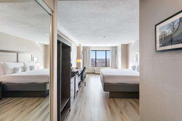 A hotel room with two beds, a desk, a chair, and a large window.