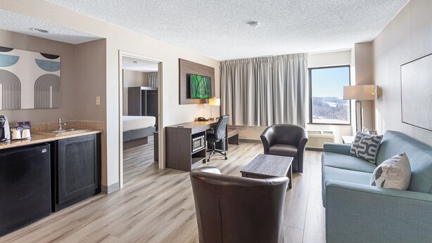 A modern hotel room with a kitchenette, a dining area, a sofa, and a TV.