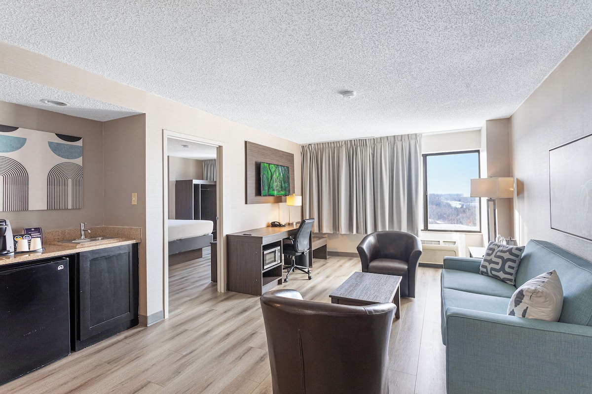 A modern hotel room with a kitchenette, a dining area, a sofa, and a TV.