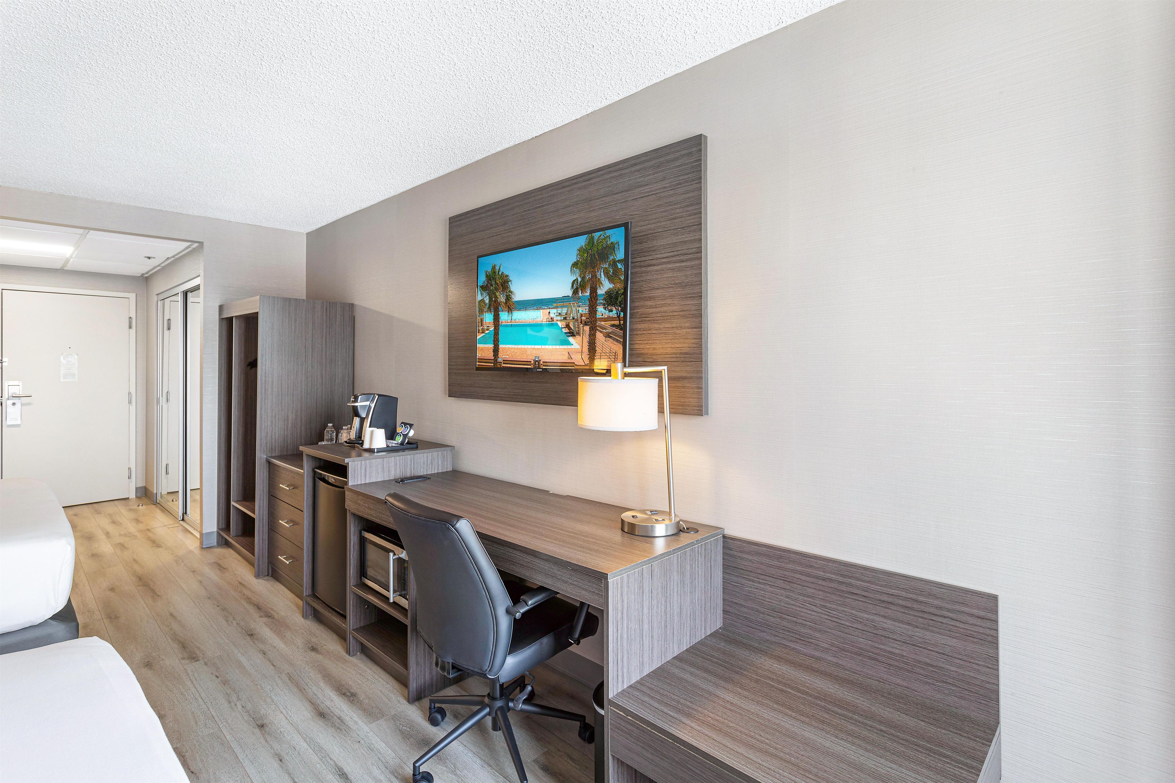A hotel room with a desk, chair, and a painting of a beach scene.