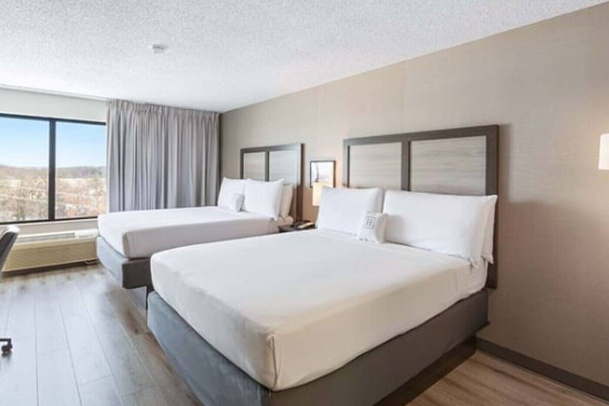 A hotel room with two beds, a large window, and a view of the city.