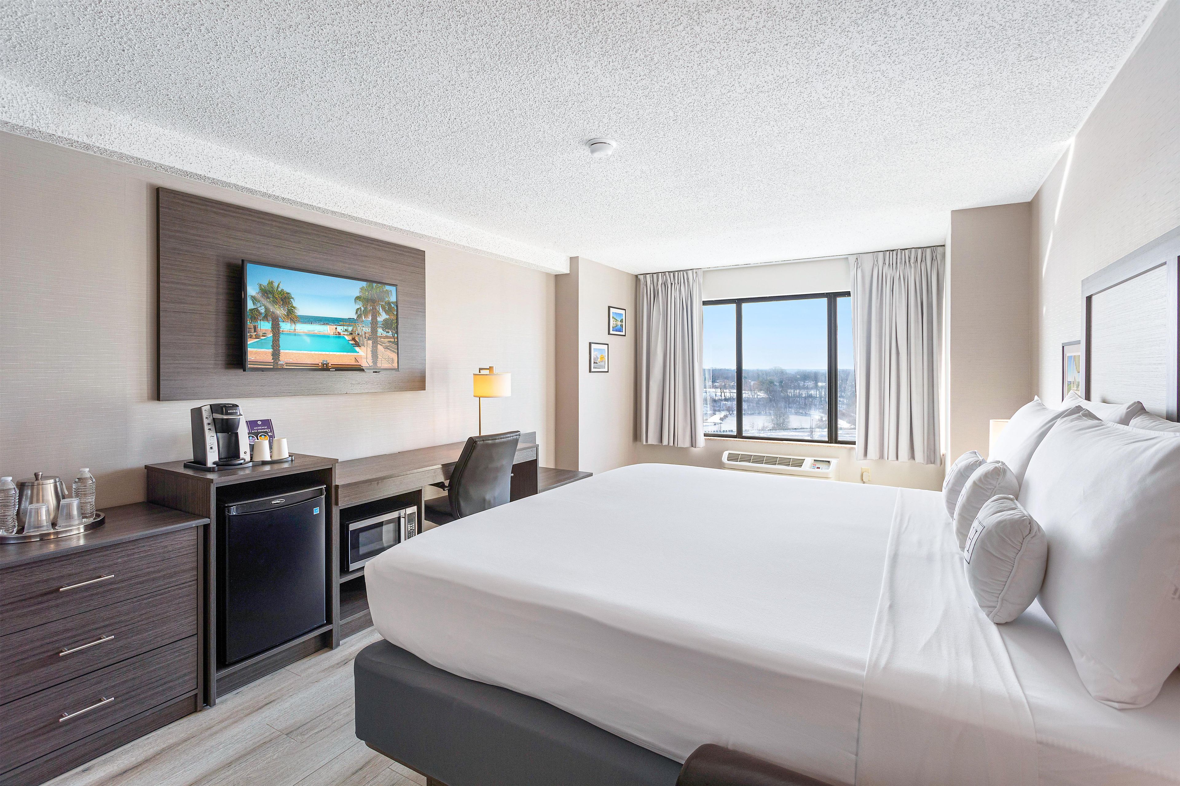 Een hotelkamer met een groot bed, een bureau met een koffieapparaat, een televisie aan de muur en een raam met uitzicht.