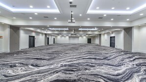 Un amplio salón de conferencias vacío con suelo de diseño marmolado, iluminación empotrada y un proyector instalado en el techo.