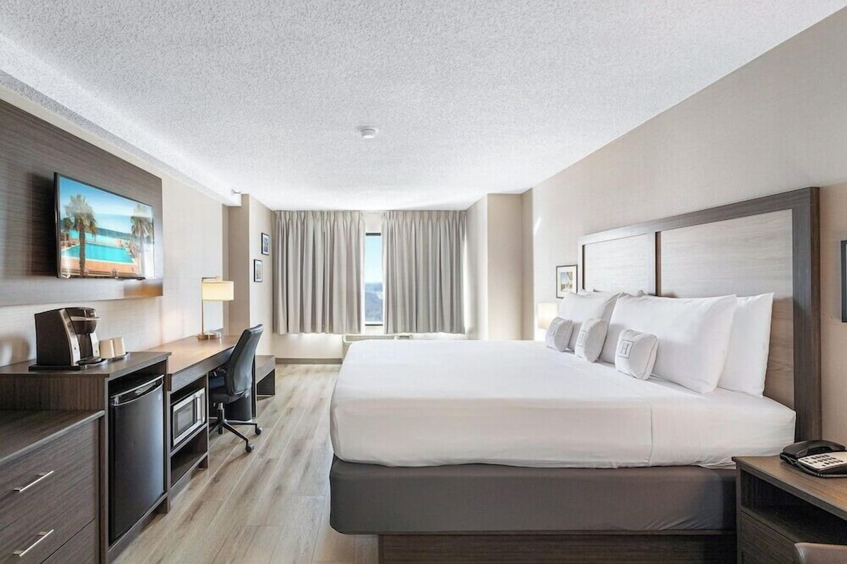 A hotel room with a large bed, a desk with a computer, a TV, and a view of the outdoors.